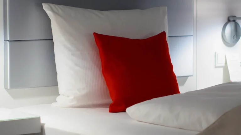 Chambre d'hôtel simple avec lit double et coussin rouge, aux murs clairs